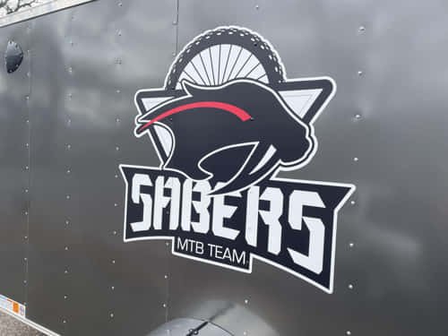A bold, custom-cut vinyl trailer decal displaying the Sabers MTB Team logo, applied to a matte black surface for professional team branding on the go.